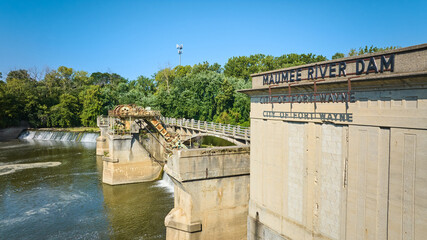 Sunny Maumee River Dam City of Fort Wayne sign on building with basin and waterfalls beneath green...