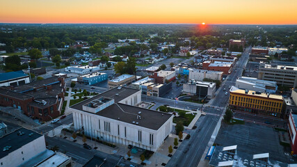 Fototapeta premium Red sun dawning over Muncie Indiana downtown buildings and courthouse at sunrise, aerial