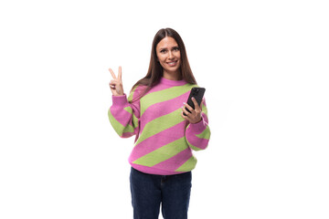 young slender caucasian woman with straight black hair dressed in a striped pink pullover communicates in social networks using a smartphone