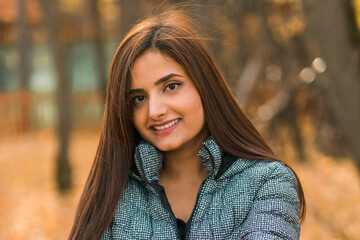 Naklejka premium Close up portrait of pretty indian young woman enjoying warm autumn sunny day vacation outdoors. Generation z and gen z concept. Fall Season