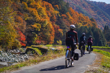 A group of cyclist enjoying riding by the river with beautiful scenery of autumn leaves in Kaida Kogen, Nagano Prefecture, Japan. (Selective focus on second cyclist)
