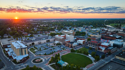 Muncie, IN sunset with golden sun over horizon aerial of downtown buildings and Canan Commons Park