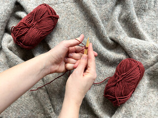 The top view of women's hands casts on loops from red woolen threads for knitting with red yarn...