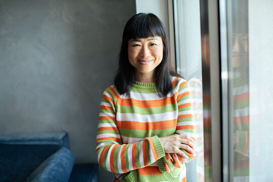 Asian woman standing in home living room looking at camera