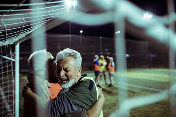 Senior Soccer Players Celebrating a Goal at Night