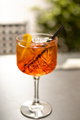 Aperol Spritz Cocktail. Alcoholic beverage based on table with ice cubes and oranges outdoors. Served cocktail with orange slice and straw placed on the table of sidewalk cafe in Italy