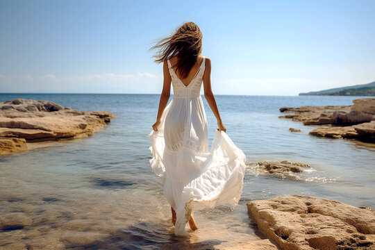 Young woman wearing white dress walking on the beach. Portrait of caucasian woman run through beach sand during sunny day. Photo from back view. Generative AI