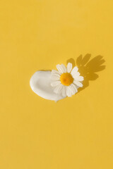 The texture of the cream with a chamomile flower on a yellow background. Smear of skincare cosmetics product. The concept of natural cosmetics. Top view