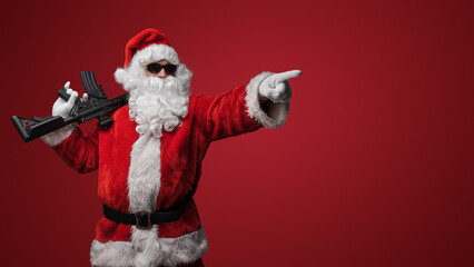 Fototapeta na wymiar A man in a Santa Claus suit, wearing black sunglasses, poses with toy guns in hand against a red backdrop