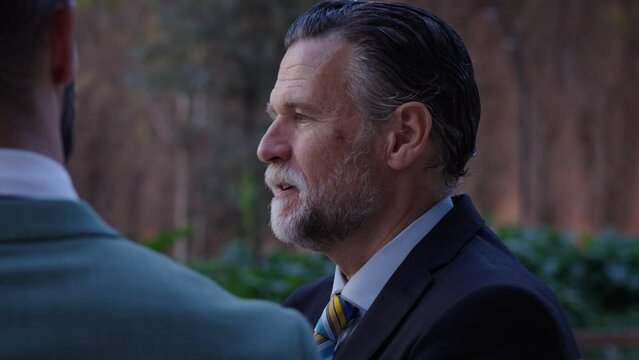 Side view mature gray business man. Two adult entrepreneur serious and calm in street outdoor. Male having conversation on break work discussing and negotiating important business issues at meeting.