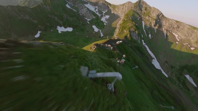 Aerial dynamic dive gorgeous green snowy ridge gazex mountains sunny summer morning nature. Cableway funicular ropeway mount slope. FPV sport drone flying down along green rock slope mountain valley