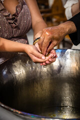 Close-up of a woman's hands above the baptistery, capturing the intricate details of the Greek Orthodox baptizing process. Selective focus.