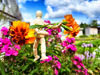 Wooden toy man with flowers against background grass in nature. Concept of holiday, gift bouquet,...