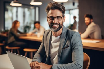 Obraz premium Happy and successful man working on laptop in office, Sitting at table in bright room, Smiling.