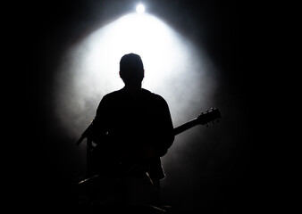 Musician playing guitar performing on stage under spot light. Silhouette of a music artist and band...