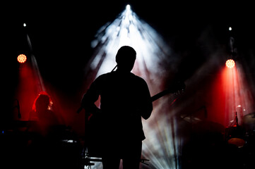Musician playing guitar performing on stage under spot light. Silhouette of a music artist and band on stage.