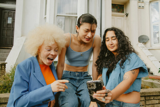 Three multiracial friends in trendy outfits looking at phone in urban area having fun