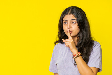 Shh be quiet please. Indian young woman presses index finger to lips makes silence gesture sign do not tells secret, stop talk gossip, confidential privacy. Arabian girl isolated on yellow background