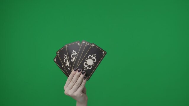 In a frame on a green background. A woman hand that holds a fan of tarot cards or playing cards, they are turned towards the camera with the outer side with a pattern. Someone is pulling one card