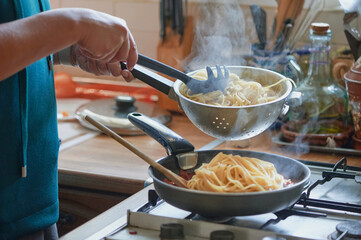 Cooking traditional recipes at home. Unrecognizable woman adds spaghetti from a wringer to a pan on...
