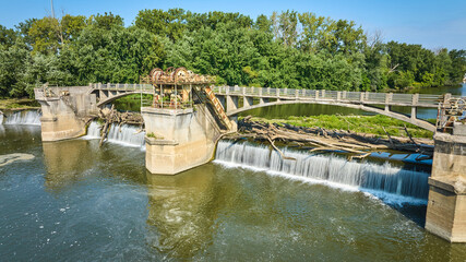 Fototapeta premium Logs over waterfalls into swirling basin at Maumee River Dam on sunny summer day aerial Fort Wayne, IN