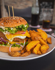 Crispy chickpea veggie burger, served with deluxe potatoes, egg, lettuce, cheese, tomato, onion. With the drink in the background. Delicious vegetarian meal.