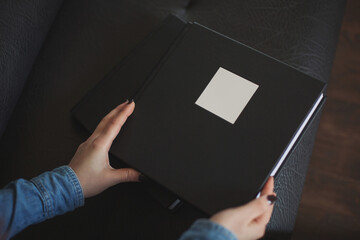 Female hands holding a beautiful leather black bound book in box with soft fabric. Wedding photo book,family album. The texture of the cover of a photobook made of genuine leather. Photobooks for gift
