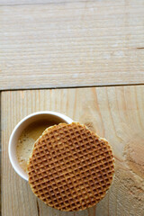 Fototapeta na wymiar One stroopwafel with one white cup of black coffee on the wooden background. A cup of coffee on the wooden table with a biscuit