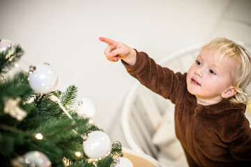 Little girl pointing with index finger at decoration hanging on Christmas tree