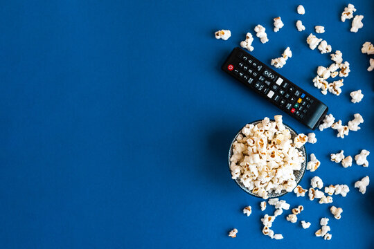 Popcorn and decorative pumpkins with TV remote on a blue background with copy space. Movie night concept. Wateching TV themed photo. Fall or autumn TV shows.