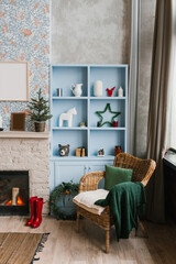 Stylish Christmas decor of Scandinavian living room with fireplace and wicker armchair, blue wardrobe decor