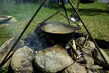 Tourists prepare lunch in hiking pot on campfire at campsite. Soup boils in cauldron.