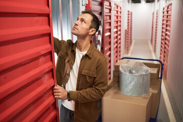 Mature man opening door of storage unit to put belongings inside when busy with relocating processes