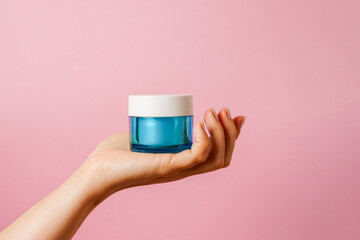 Elegant female hand holding blue glass jar of cosmetic cream on pink background. copy space