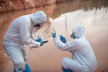 Two men wore PPE suits. One of them sat down and held up a glass bottle containing contaminated...