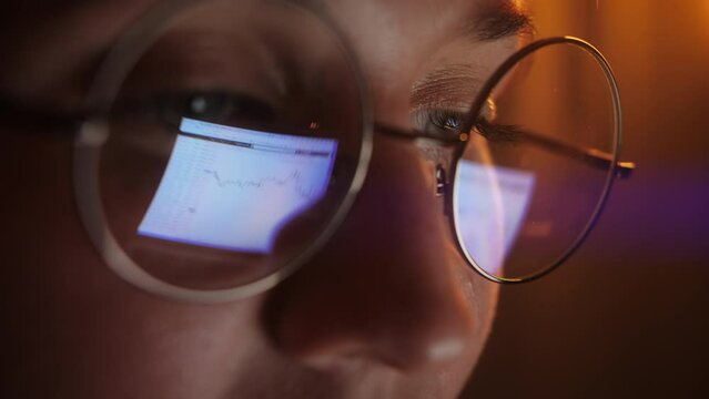 Eyes in glasses late at night close up. Coder, programmer or developer using laptop in dark. Close up of glasses with reflection of computer screen.