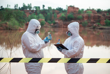 Two men wearing PPE stood holding glass bottles filled with contaminated water and attempting to analyze the water.