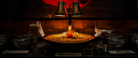 Classic Spanish paella with shrimps, clamps, mussels in traditional pan displayed on buffet line in restaurant for catering wedding, birthday party or other event - obrazy, fototapety, plakaty