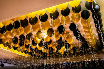 Black and yellow helium filled balloons under ceiling. Festive decoration for wedding, anniversary, birthday celebration or other event