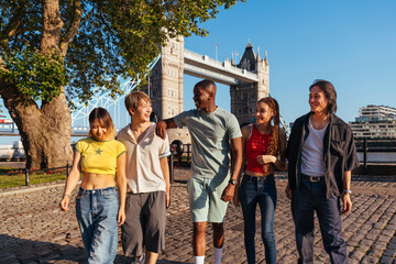 Obraz premium Multiracial group of happy young friends bonding in London city - Multiethnic teens students meeting and having fun in Tower Bridge area, UK - Concepts about youth lifestyle, travel and tourism