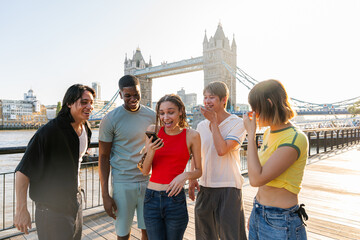Obraz premium Multiracial group of happy young friends bonding in London city - Multiethnic teens students meeting and having fun in Tower Bridge area, UK - Concepts about youth lifestyle, travel and tourism
