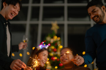 men and women holding sparkler fireworks in a party with Christmas tree. young couple Asian people...