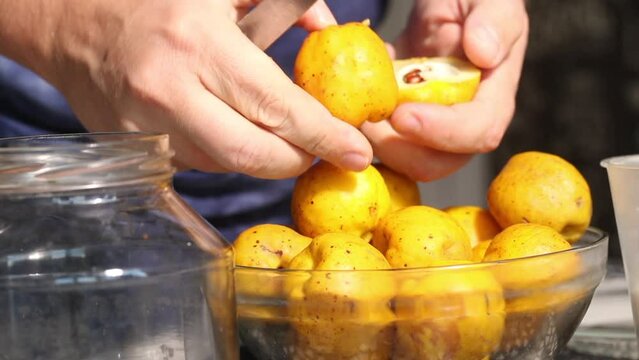 A man cuts yellow quince fruits with a knife. Removes seeds from them. Crush the fruits into a jar. Prepares quince liqueur. Close-up.