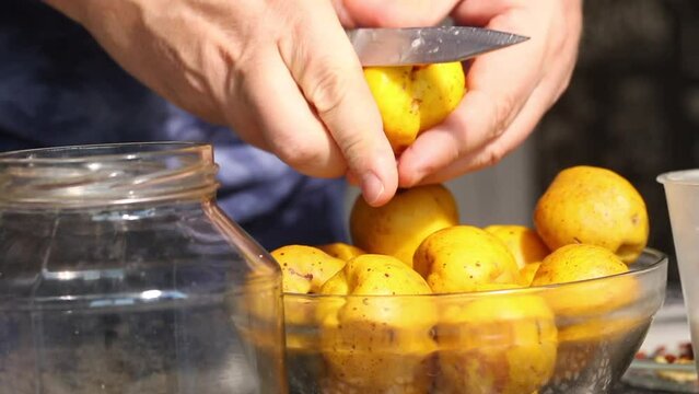 A man cuts yellow quince fruits. Removes seeds from fruits. Crush the fruits into a glass jar. There is sugar in a glass nearby. Prepares quince liqueur. Close-up.
