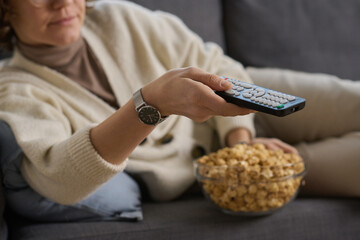 Close-up of young woman lying on sofa and using remote control to watch TV with popcorn