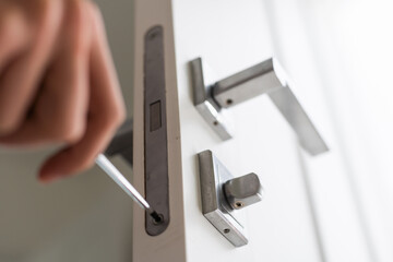 A locksmith is repairing an interior door lock. Close-up of male hands repairing or replacing an entrance door lock with a hex screwdriver