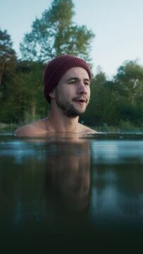 Serious man chills and shakes while standing inside cold winter lake at morning