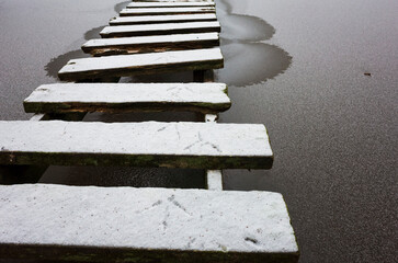 Tracks of a gray heron on an old wooden bridge dusted with fresh snow over ice-covered gray water...