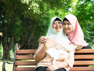 Happy muslim young daughter hugging with senior mother wearing hijab sitting on bench at park. Mother day concept. family concept