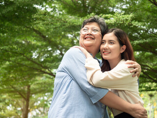 Fototapeta premium Happy smiling young daughter hugging with senior mother at park and looking forward. Mother day concept. family concept
